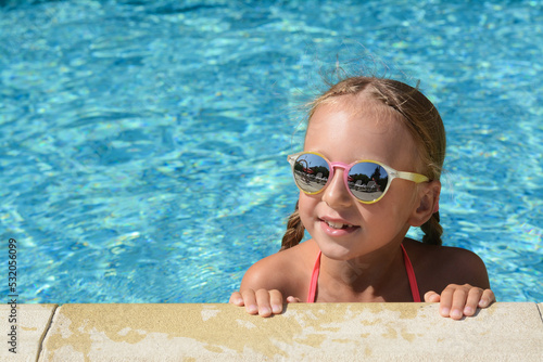 Happy cute little girl with sunglasses at edge of swimming pool on sunny day. Space for text