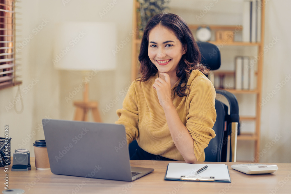 Portrait of a beautiful Asian woman looking at laptop screen while sitting at working desk in the office Portrait of a beautiful Asian woman looking at laptop screen while sitting at working desk in the office