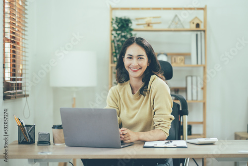Portrait of a beautiful Asian woman looking at laptop screen while sitting at working desk in the office