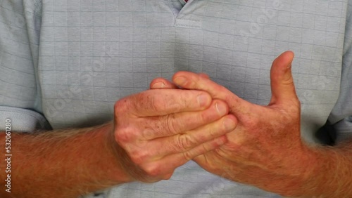 Close-up of adult caucasian male massaging left hand fingers with his right hand fingers. Mature white man wearing a blue shirt rubbing his sore left hand fingers with his right hand fingers close-up.