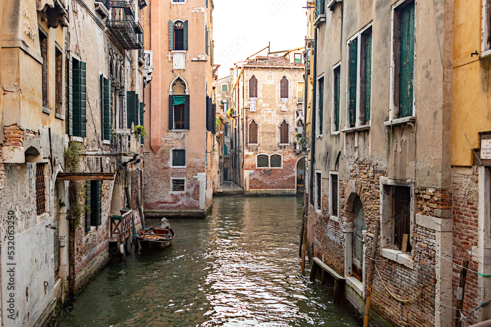 Narrow canal with medieval buildings, stone walkway and bridge reflected in calm water  in Venice, Italy on sunny day.