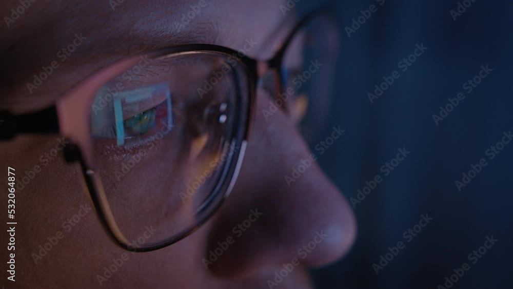 man with glasses works at a computer in the evening at home, glare on