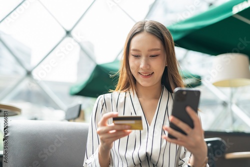 Close up photo of young asian beautiful female lady making a payment for an online shopping purchase via her smart phone easily and successful while sitting in a cafe photo