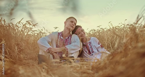 Man and a woman Slavs are sitting in a field, a woman put her head on a man's shoulder. Loving couple of Slaves are resting in the field and dreaming. Beautiful landscape with golden ears. 4k, ProRes