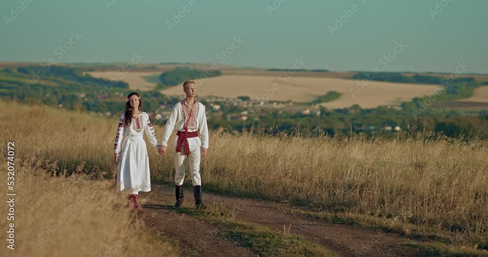 Young Slaves are walking along a rural road and holding hands, friendship of peoples. Man and a woman in national costumes are walking around the village, they are happy. 4k, ProRes Young Slaves are walking along a rural road and holding hands, friendship of peoples. Man and a woman in national costumes are walking around the village, they are happy. 4k, ProRes