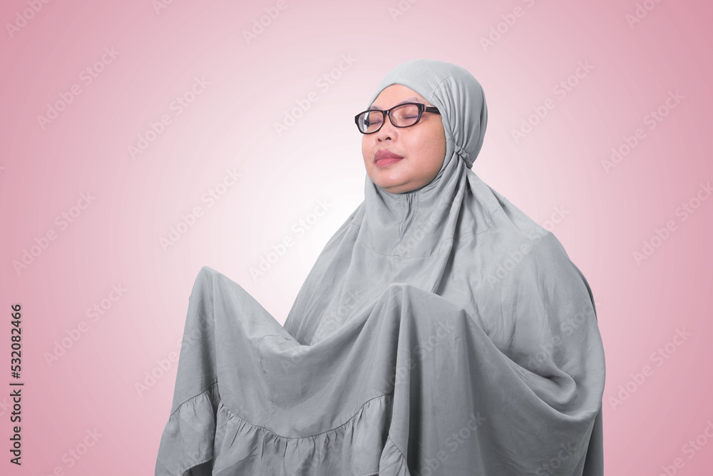 Portrait of Asian woman wearing prayer gown or mukena while praying with hands raised. Isolated image on white background Portrait of Asian woman wearing prayer gown or mukena while praying with hands raised. Isolated image on white background