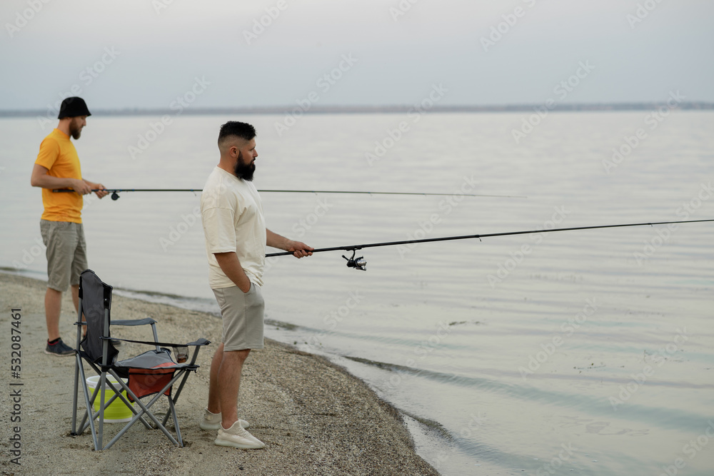Two friends with fishing rods fishing at sea. leisure and people