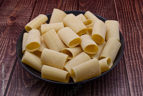 Traditional Italian uncooked Paccheri Pasta from Gragnano on wooden table.