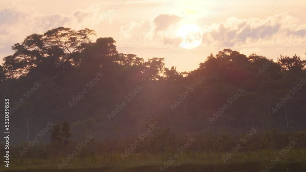 Tilt up showing the reflection shimmering on water to the sun in the sky hidden behind the clouds over the amazon rain forest Tilt up showing the reflection shimmering on water to the sun in the sky hidden behind the clouds over the amazon rain forest