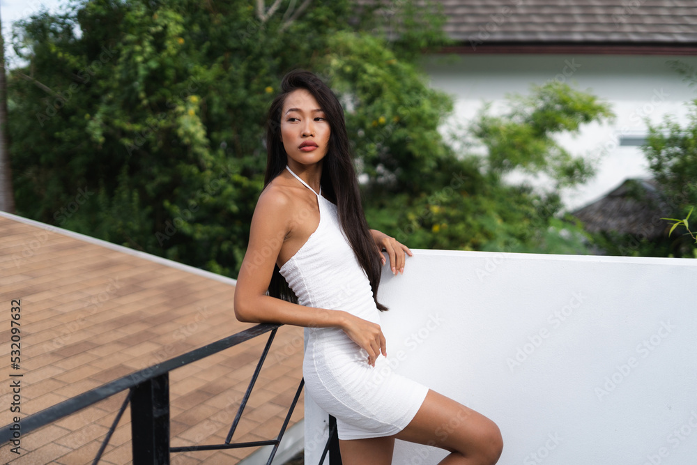 Beautiful asian thai woman with soft smooth clean dark tanned skin posing outdoor in white dress with tropical background Beautiful asian thai woman with soft smooth clean dark tanned skin posing outdoor in white dress with tropical background