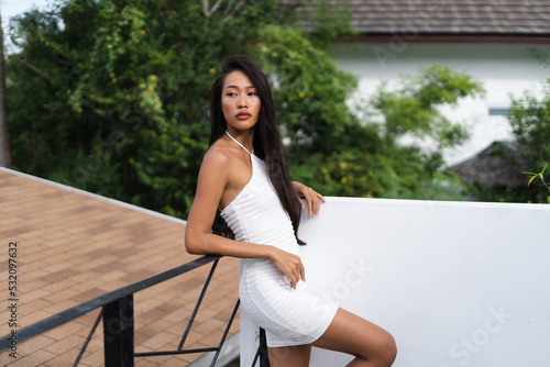 Beautiful asian thai woman with soft smooth clean dark tanned skin posing outdoor in white dress with tropical background