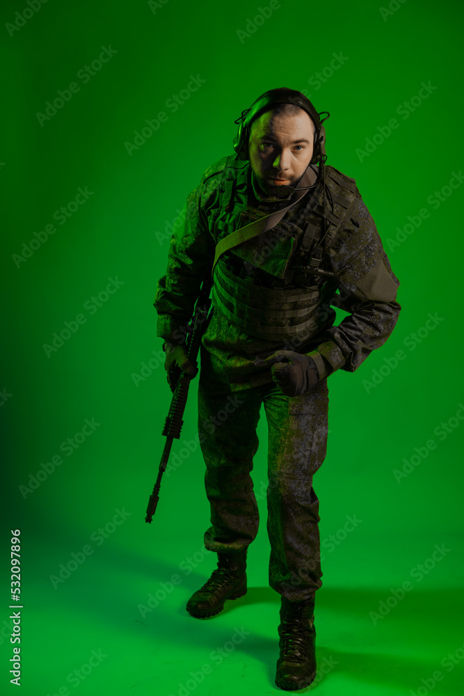 soldier in the studio on a green background with colored light. a man in military uniform with a gun, rifle or machine gun. military. airball player soldier in the studio on a green background with colored light. a man in military uniform with a gun, rifle or machine gun. military. airball player