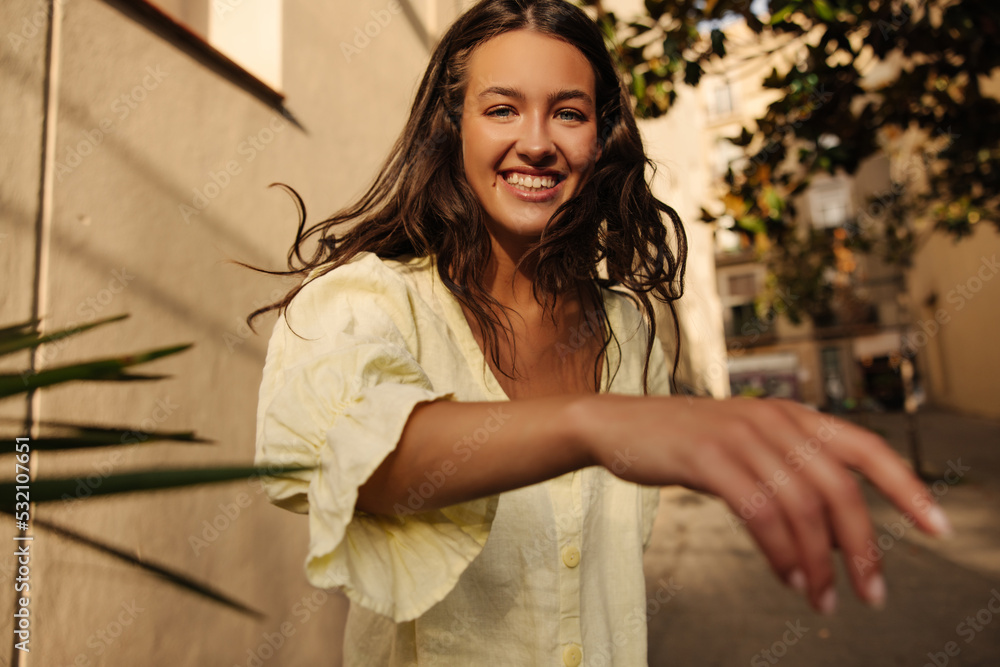 Fototapeta premium Cheerful young caucasian brunette girl resting outdoors on weekends in warm weather. Lady smiles, wears summer sundress. Lifestyle concept