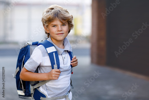 Happy little kid boy with backpack or satchel called Ranzen in German. Schoolkid on way to school. Portrait of healthy adorable child outdoors. Student, pupil, back to school. Elementary school age