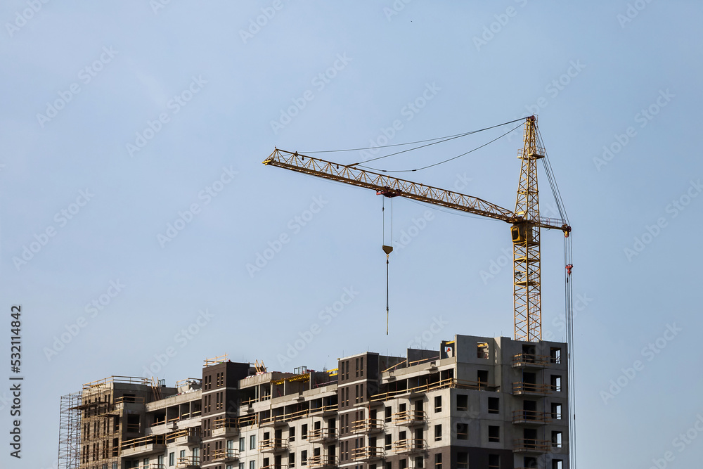 Construction crane work on creation site against blue sky background. Bottom view of industrial crane. Concept of construction of apartment buildings and renovation of housing. Copy text space