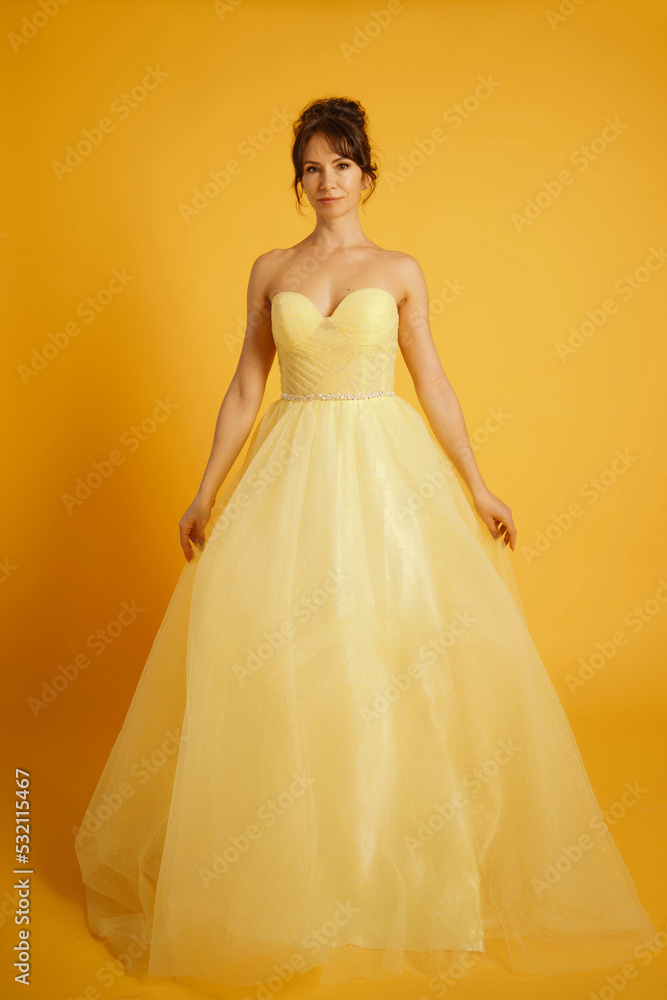 Fototapeta premium Portrait of a beautiful middle-aged woman in a yellow dress, her hair pulled up against a yellow background