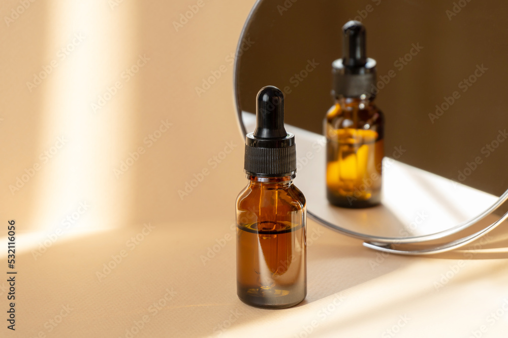 Cosmetic serum for face in glass bottle on beige background in rays of sunlight. Dry skin care product, essential oil for moisturizing skin is reflected in mirror. Copy space, close-up Cosmetic serum for face in glass bottle on beige background in rays of sunlight. Dry skin care product, essential oil for moisturizing skin is reflected in mirror. Copy space, close-up