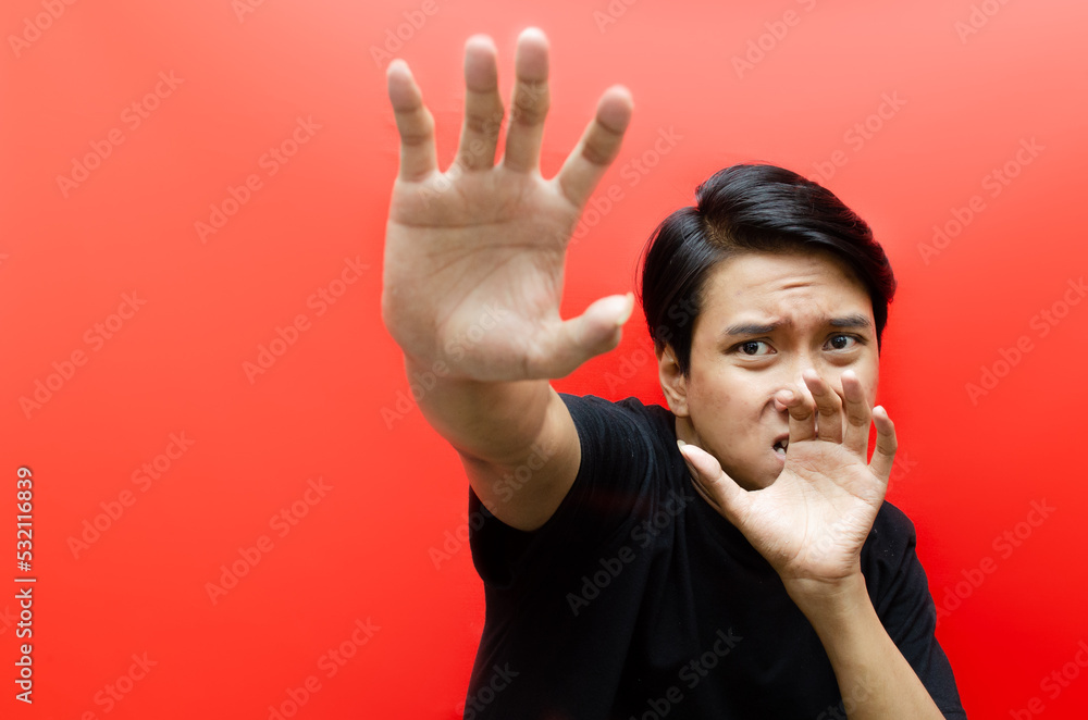 Naklejka premium asian man making frightened gestures with his palms as if trying to defend himself from someone while having a terrified expression on his face.