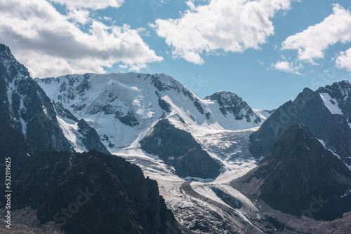 Atmospheric landscape with large snow mountain range in sunny day. Glacier and icefall in bright sun among sharp rocks. Awesome view to high snowy mountains. Snow-covered mountain wall with glacier.
