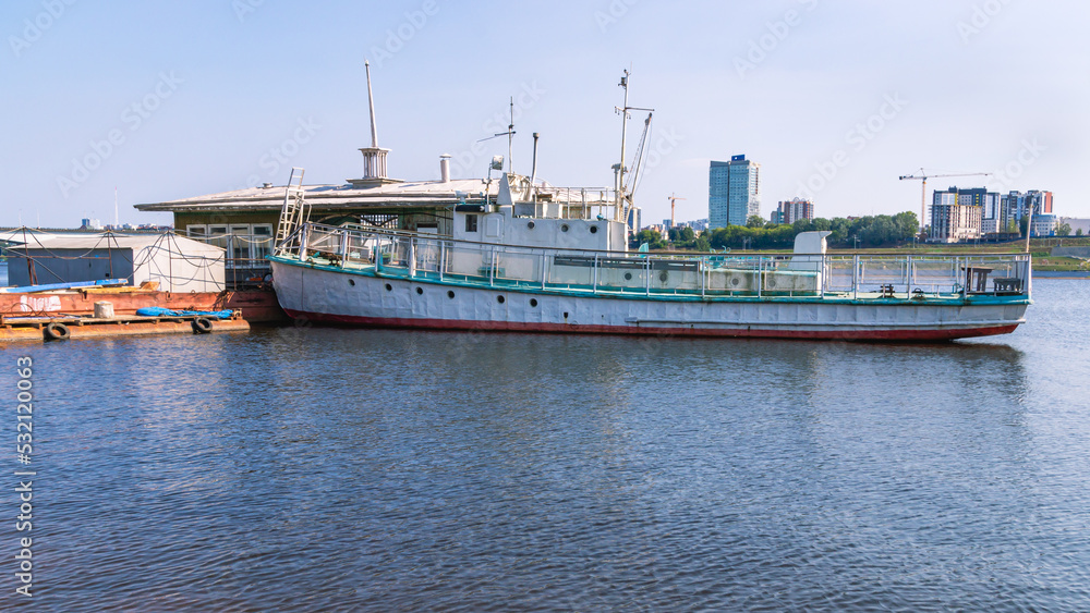 An old ship on the river, moored to a floating pier. View of the old river steamer. River navigation.