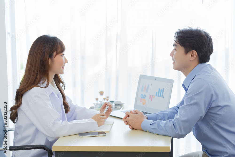 Female doctor and young male patient while consult and explain. Doctor and patient sitting together at table in examination room.