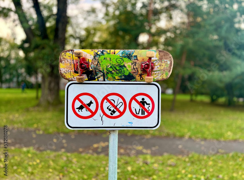 No smoking, no dogs, and no littering sign at the skate park with a used skateboard on it