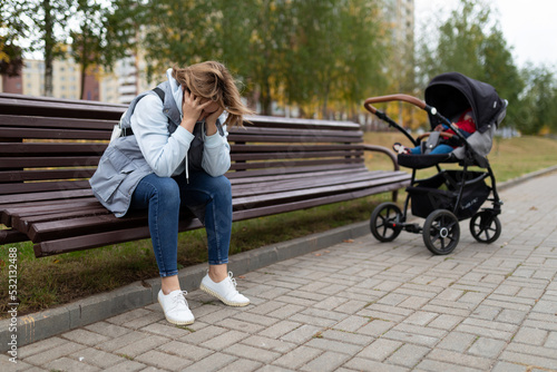 a young mother sits on a bench upset next to a baby stroller, Concept of postpartum depression photo