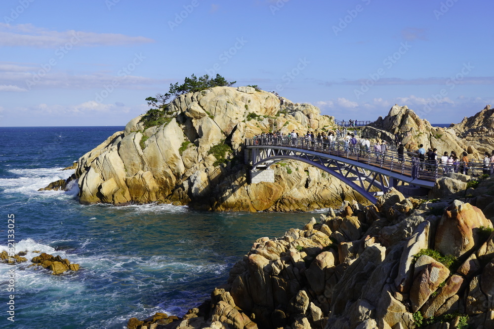 Obraz premium Beautiful view of the bridge with people located on rocks at top of blue sea at Ulsan beach, South Korea