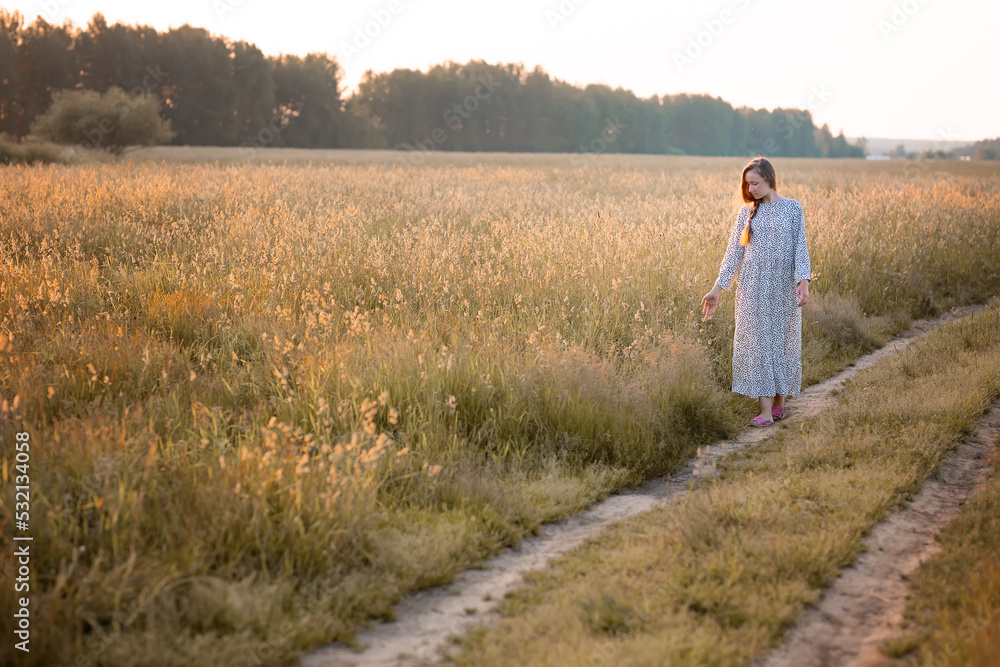 A young woman in a field at sunset. The girl walks across the field in the rays of the sun and touches the grass. The concept of freedom and a rich harvest.