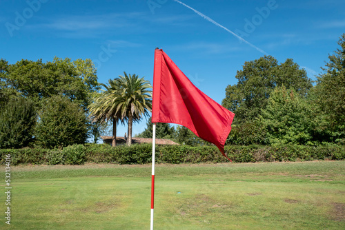 Campo de golfe rodeado por árvores e a bandeira vermelha sobre o relvado photo