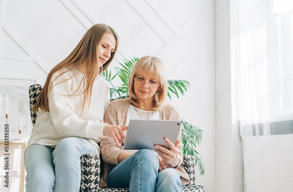 Senior woman and daughter playing with tablet pc. Smiling older woman and her granddaughter sitting home using gadget digital device for online shopping internet surfing video conference calling. Senior woman and daughter playing with tablet pc. Smiling older woman and her granddaughter sitting home using gadget digital device for online shopping internet surfing video conference calling.
