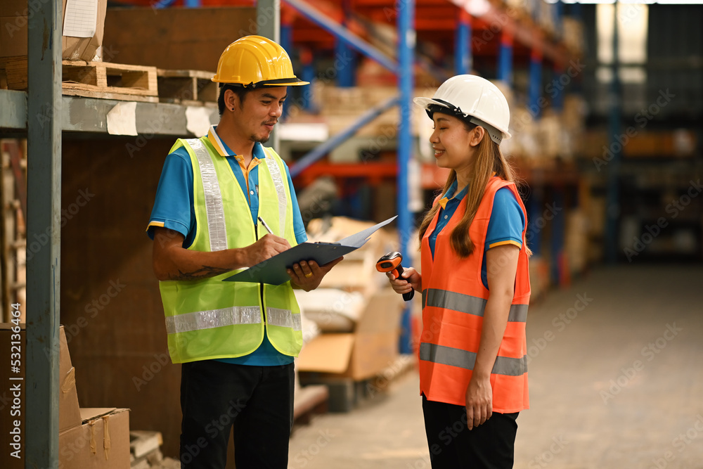 Warehouse workers in safety uniform working in warehouse full of tall shelves with goods in cardboard boxes Warehouse workers in safety uniform working in warehouse full of tall shelves with goods in cardboard boxes