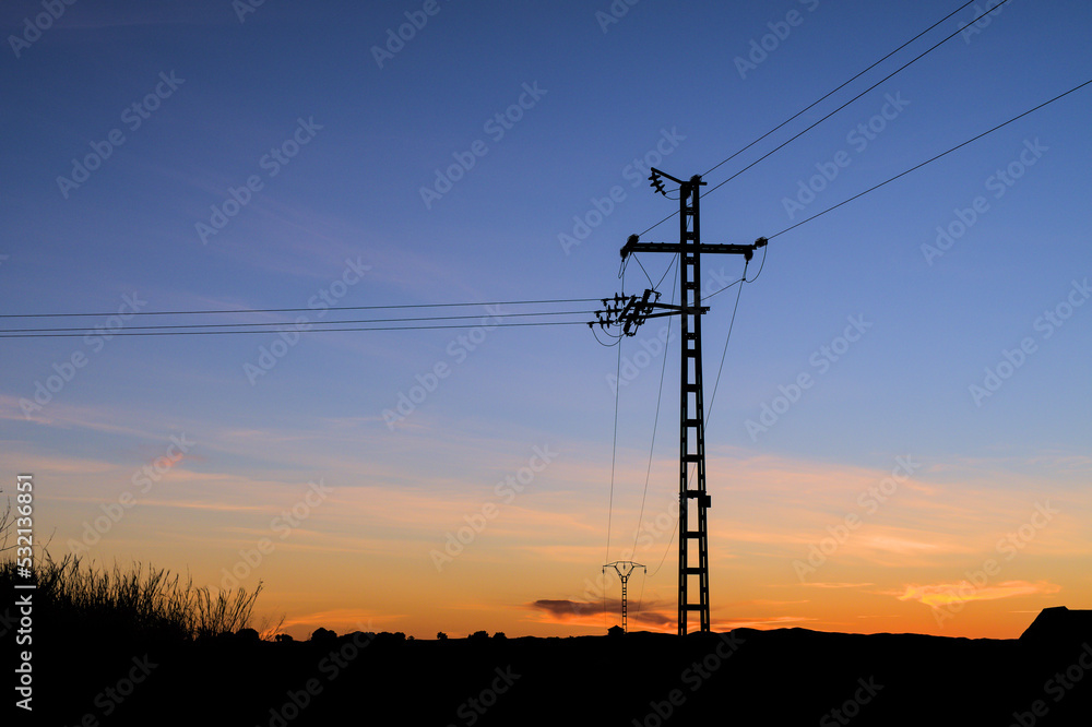 Silhouette of an electric pole on dusk background. Sunset over the electric power lines. Clean energy. High voltage electric power tower. 
