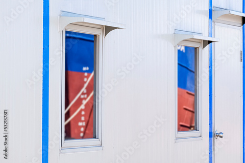 Side view of 2 glass windows on white wall of office container in commercial dock area