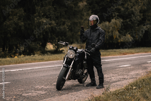 male biker motorcyclist holding a smartphone in gloves in autumn on a motorcycle cafe racer on a journey.
