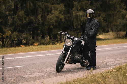 male motorcyclist in a warm jacket and helmet in cold autumn weather on the road with a motorcycle cafe racer © velimir