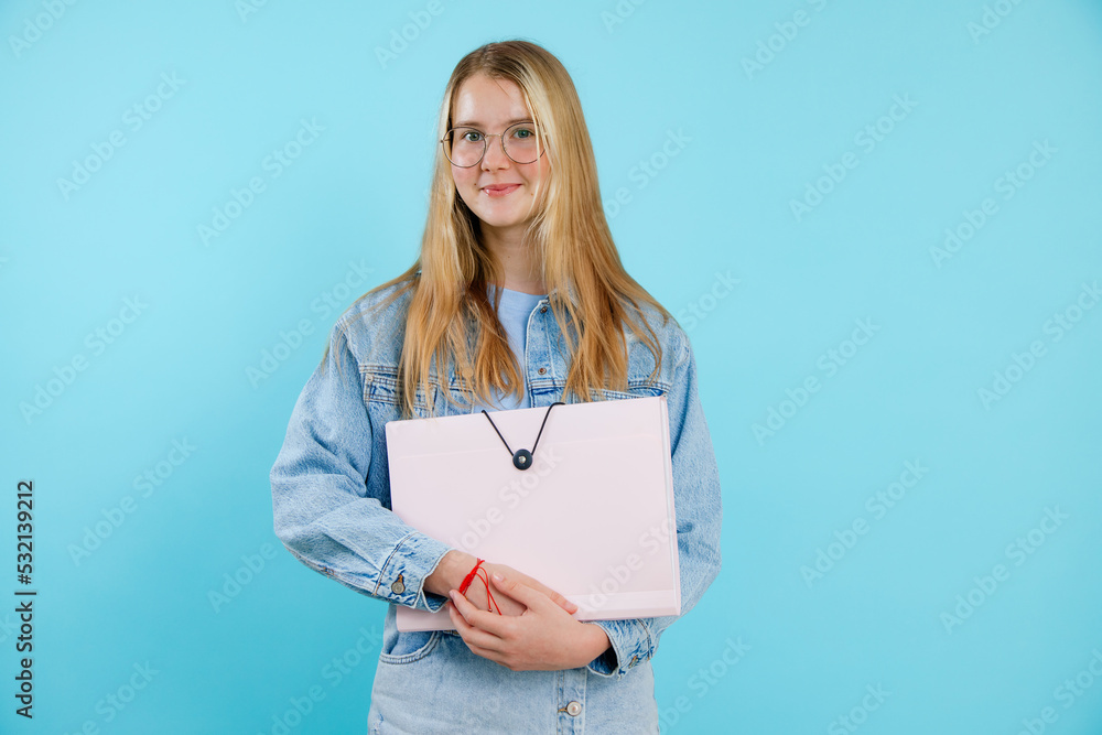 Confident, powerful, smiling blonde teenage girl in glasses holding paper folder, portfolio. Back to school, university Confident, powerful, smiling blonde teenage girl in glasses holding paper folder, portfolio. Back to school, university