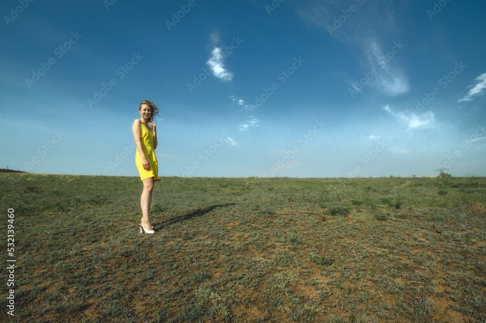 attractive lady in yellow sundress posing on the green meadow against the blue ultramarine sky