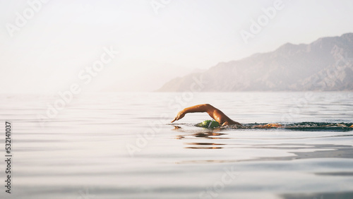 Professional swimmer woman swimming open water at sunrise sea