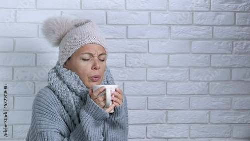 Lady feeling discomfort in clothes indoor. A young lady in winter cap try to get warm with hot bevarage in cold apartment. A concept of household debts and rising prices for heating in Europe. photo