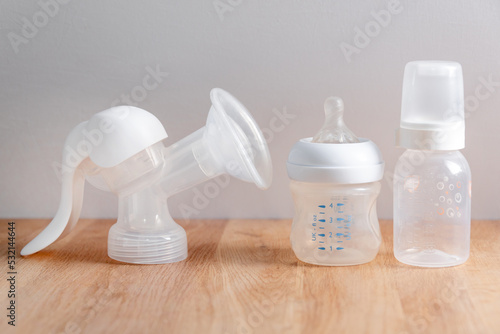 Manual breast pump and nursing bottles for newborn baby on wooden table. Device for increasing milk supply for breastfeeding mother. Maternity, baby care concept. photo