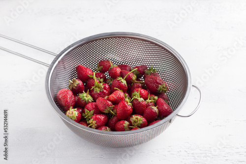 Metal colander with washed organic strawberries on a light gray table