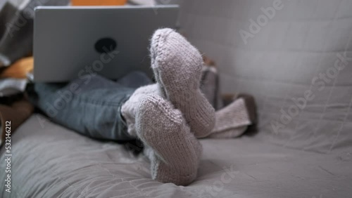 Girl in warm socks with notebook. A teen try to get warm in knitted grey socks with her notebook on sofa during winter unheated period. photo