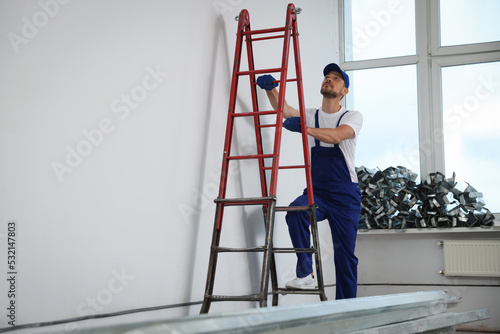 Construction worker climbing up stepladder in room prepared for renovation