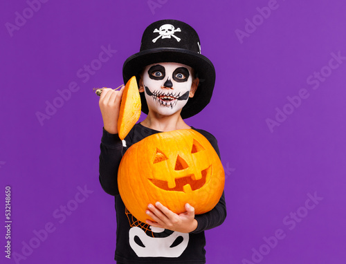 Happy cheerful boy in skeleton costume with  pumpkin  jack-o-lantern celebrates Halloween and laughs on purple background