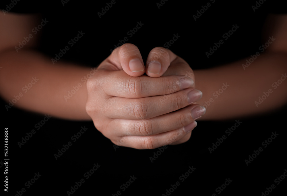Woman holding hands clasped while praying against black background, closeup Woman holding hands clasped while praying against black background, closeup