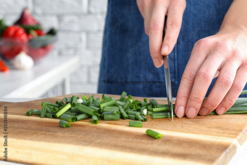 Woman cutting green spring onion on wooden board, closeup Woman cutting green spring onion on wooden board, closeup
