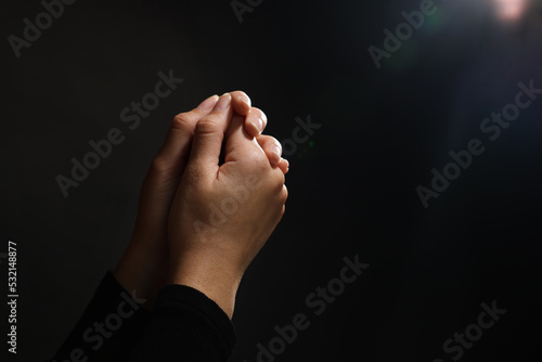 Fototapet Woman holding hands clasped while praying against light in darkness, closeup