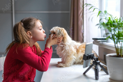 A little girl plays with a dog at home, talking on the phone online via video link