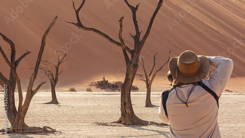 A tourist in a hat photographs petrified camel acacias in Deadvlei Valley. Namibia
